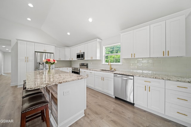 412 Apple Valley Rd, Sevierville, TN 37862 - kitchen with stainless steel appliances, white cabinetry, a kitchen breakfast bar, vaulted ceiling, and decorative backsplash