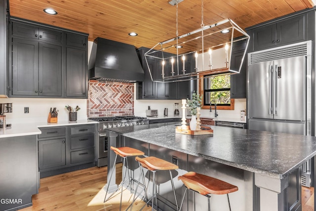 kitchen featuring wooden ceiling, decorative light fixtures, a kitchen bar, custom range hood, and high end appliances