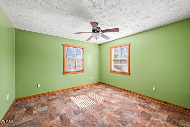 spare room with baseboards, ceiling fan, plenty of natural light, and stone finish floor