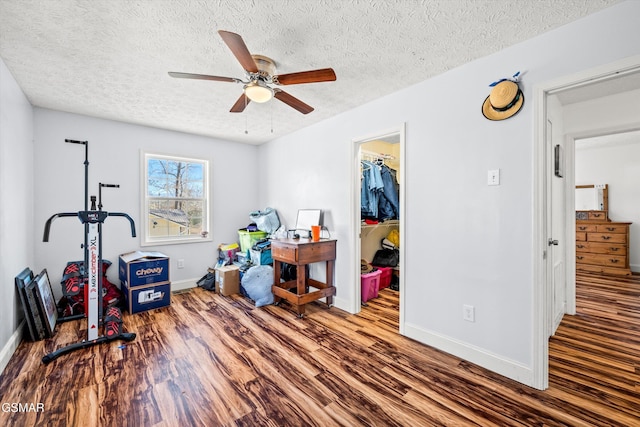 exercise room with baseboards, a ceiling fan, a textured ceiling, and wood finished floors