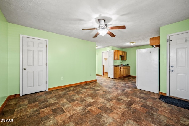unfurnished living room featuring baseboards, ceiling fan, stone finish flooring, and a sink