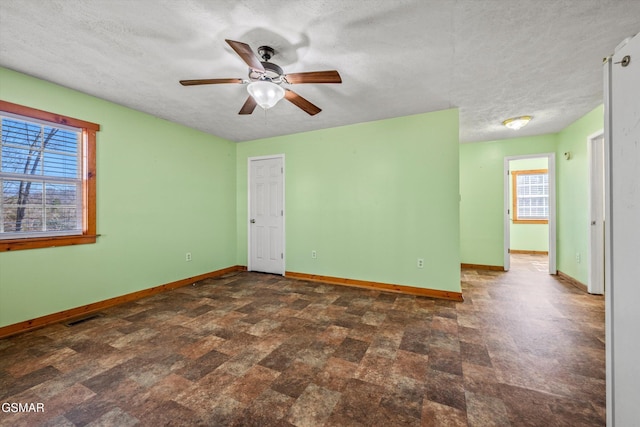 empty room with a textured ceiling, baseboards, visible vents, and ceiling fan