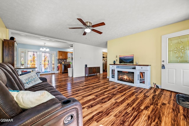 living area with a textured ceiling, a warm lit fireplace, wood finished floors, and ceiling fan with notable chandelier