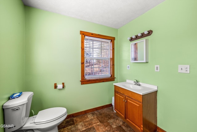 half bathroom with baseboards, vanity, toilet, and stone finish flooring