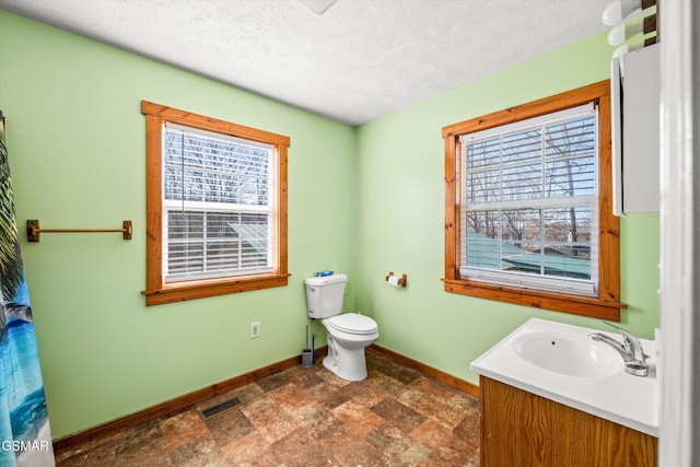full bathroom with stone finish flooring, a textured ceiling, baseboards, vanity, and toilet