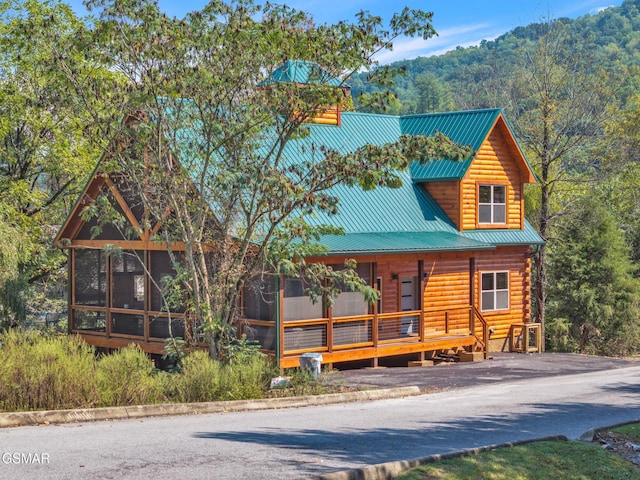 view of front of house with a sunroom, metal roof, a mountain view, log siding, and driveway