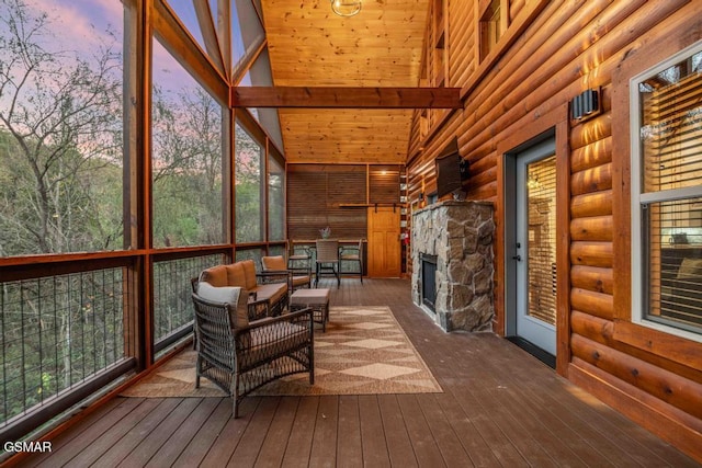 unfurnished sunroom with lofted ceiling with beams, a stone fireplace, and plenty of natural light