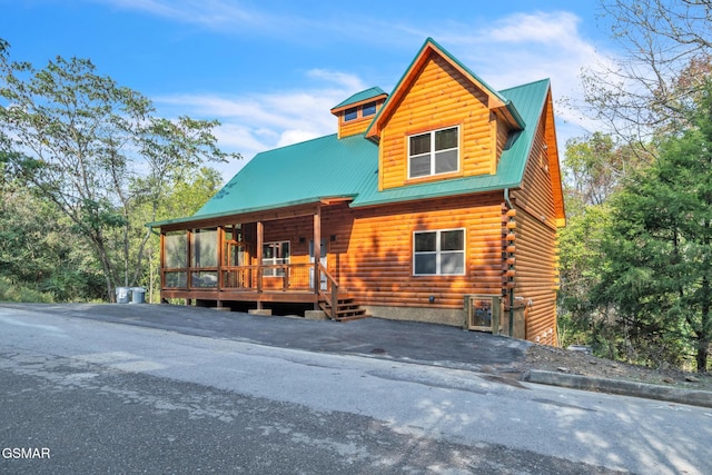 log-style house with covered porch, metal roof, log exterior, and aphalt driveway