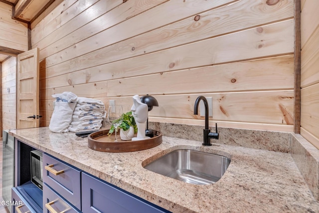 kitchen with light stone counters, a sink, wooden walls, and blue cabinetry