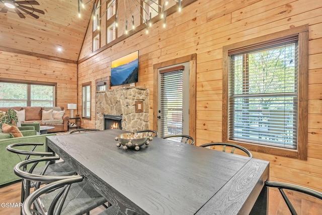 dining space with high vaulted ceiling, a stone fireplace, wooden walls, and a ceiling fan