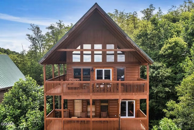 back of property with a balcony, log exterior, and a view of trees