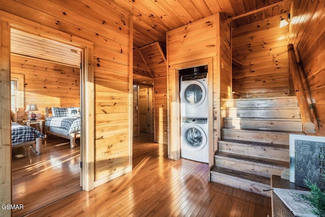 clothes washing area featuring stacked washer / dryer, wood walls, wood-type flooring, and wood ceiling