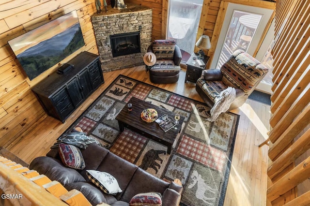 living area featuring hardwood / wood-style floors, wood walls, and a stone fireplace