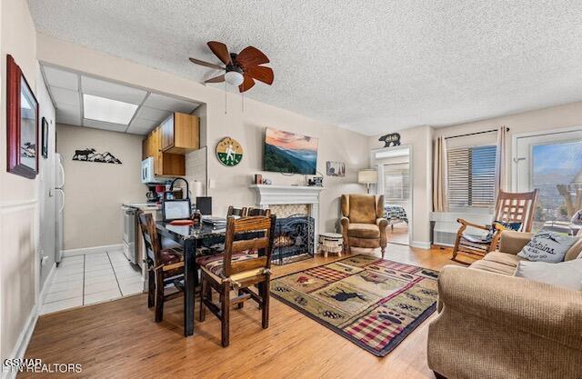102 Baskins Creek Byp Unit 104, Gatlinburg, TN 37738 - dining room featuring a ceiling fan, a textured ceiling, a warm lit fireplace, baseboards, and light wood-style floors