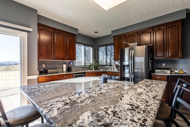 kitchen featuring light stone counters, stainless steel fridge with ice dispenser, black electric cooktop, and a center island