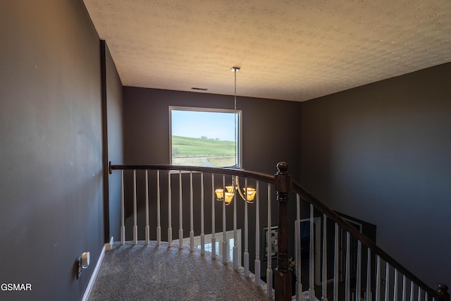 staircase featuring carpet, a notable chandelier, and a textured ceiling