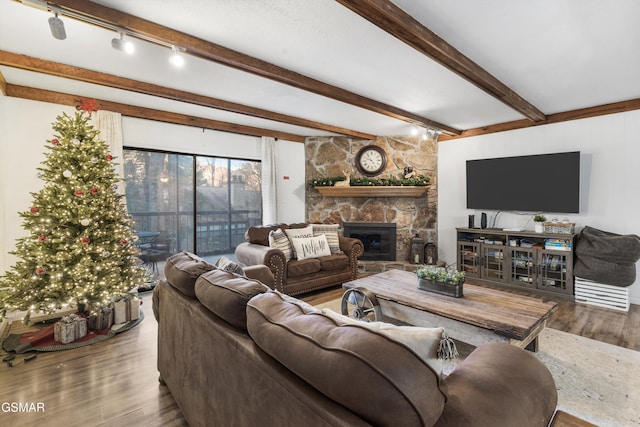 living room featuring a stone fireplace, beamed ceiling, wood-type flooring, and rail lighting