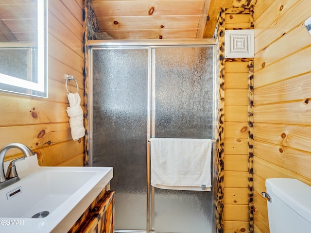 bathroom with a shower with door, vanity, wooden walls, and toilet