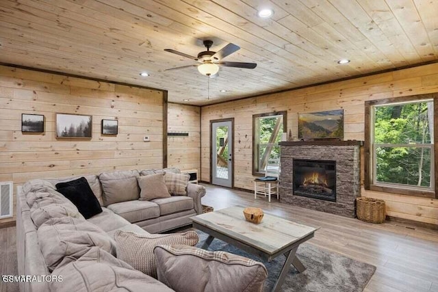 living room with a stone fireplace, wood walls, wood-type flooring, wooden ceiling, and ceiling fan