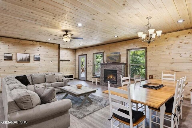 living room with wood ceiling, wooden walls, hardwood / wood-style flooring, ceiling fan with notable chandelier, and an outdoor stone fireplace