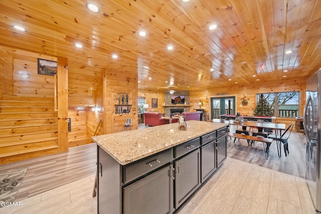 kitchen with stainless steel fridge, a center island, light stone counters, and wooden walls