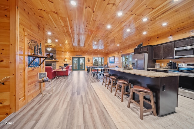 kitchen with light stone countertops, a kitchen breakfast bar, a spacious island, appliances with stainless steel finishes, and light wood-type flooring