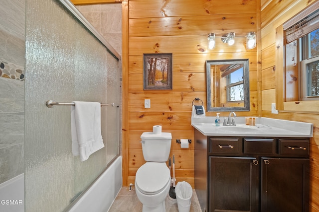 full bathroom with vanity, wood walls, tile patterned floors, bath / shower combo with glass door, and toilet