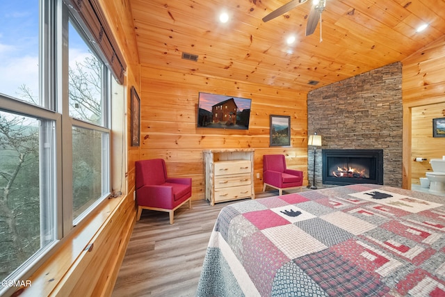 bedroom with ceiling fan, wood walls, a stone fireplace, and wooden ceiling