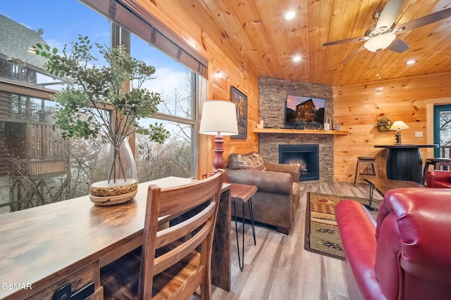 living room featuring wooden ceiling, wooden walls, an outdoor stone fireplace, ceiling fan, and light wood-type flooring