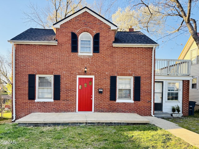 view of front facade featuring a chimney, a front yard, brick siding, and roof with shingles