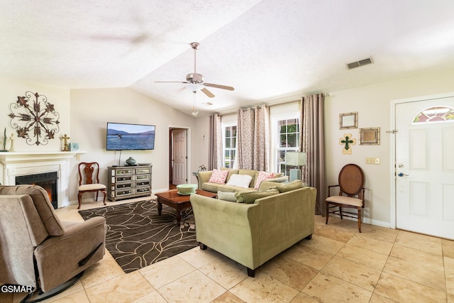 living area with a warm lit fireplace, ceiling fan, a textured ceiling, lofted ceiling, and visible vents