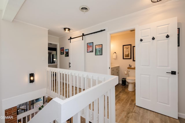 interior space with crown molding, a barn door, visible vents, light wood-style floors, and baseboards