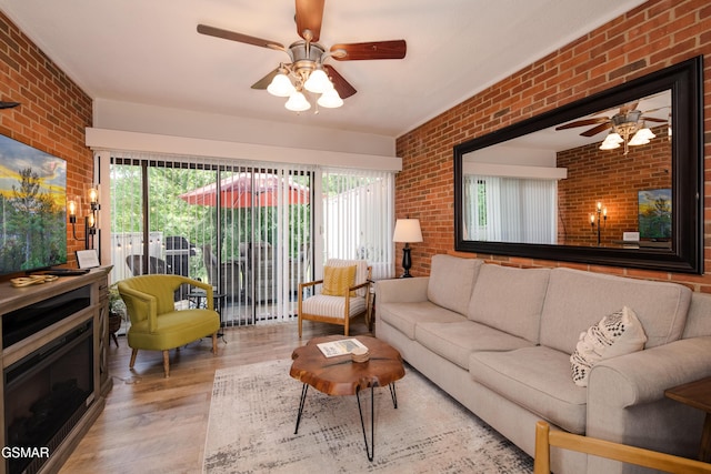 living room featuring plenty of natural light, ceiling fan, wood finished floors, and brick wall