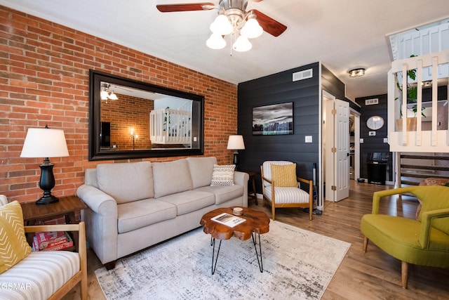 living area featuring a ceiling fan, visible vents, wood finished floors, and brick wall