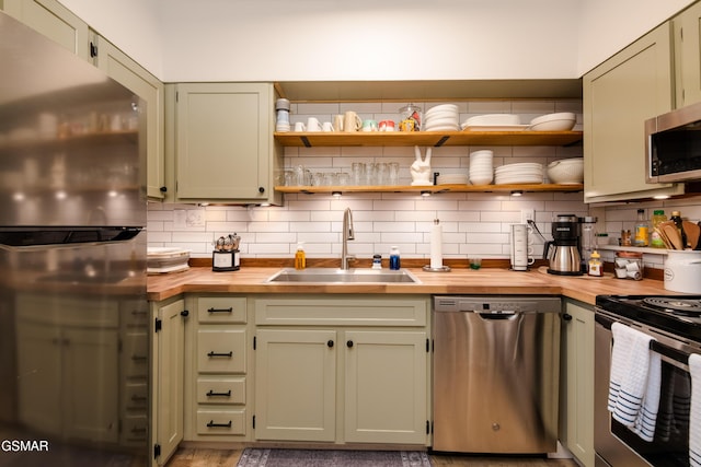 kitchen with tasteful backsplash, butcher block countertops, green cabinetry, appliances with stainless steel finishes, and a sink