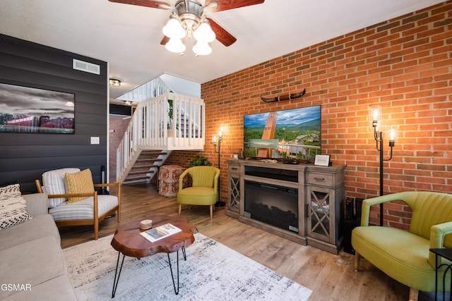 living room featuring visible vents, brick wall, wood finished floors, a ceiling fan, and stairs