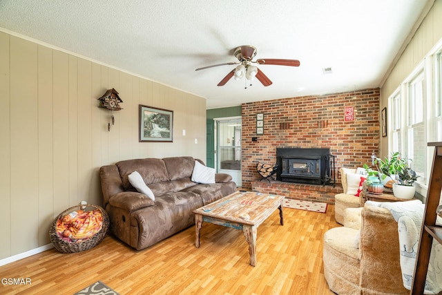 living room with ceiling fan, a textured ceiling, light hardwood / wood-style flooring, and a wood stove