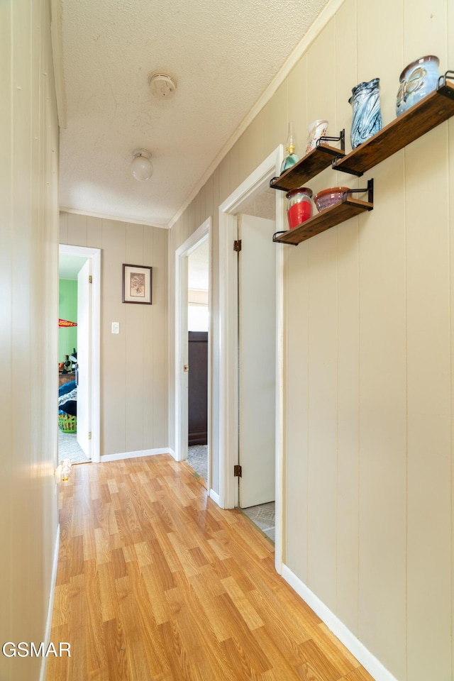 hallway featuring crown molding, light hardwood / wood-style flooring, and a textured ceiling