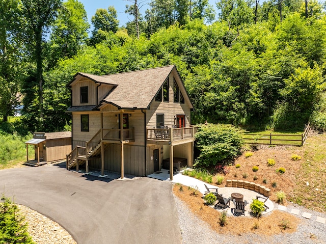 rustic home with an outdoor fire pit, a wooden deck, aphalt driveway, stairs, and an outdoor structure