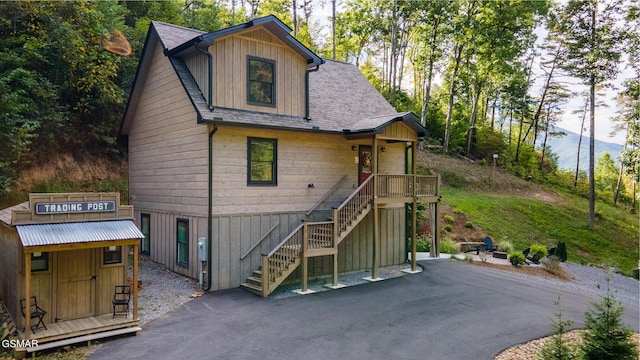 view of front facade featuring a shingled roof, aphalt driveway, an outbuilding, stairs, and a shed