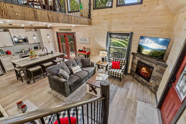 living room featuring sink, wood walls, high vaulted ceiling, light hardwood / wood-style flooring, and a fireplace