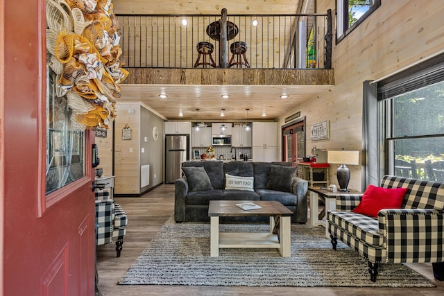 living room with a high ceiling, wood-type flooring, wooden ceiling, and wood walls