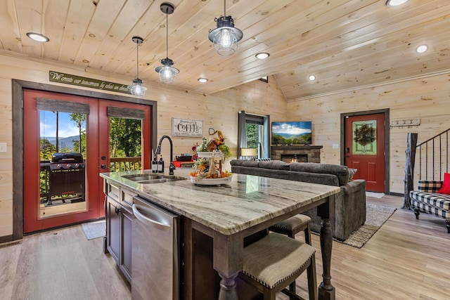 kitchen featuring sink, decorative light fixtures, wooden walls, and an island with sink