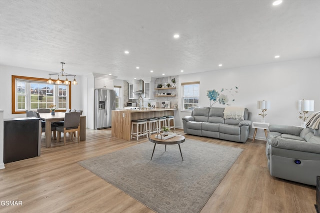 living room with light wood-type flooring, a notable chandelier, a wealth of natural light, and sink