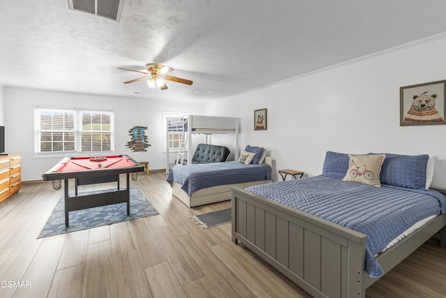 bedroom with ceiling fan, light wood-type flooring, crown molding, and a textured ceiling