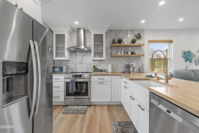 kitchen featuring butcher block counters, sink, white cabinets, wall chimney exhaust hood, and appliances with stainless steel finishes