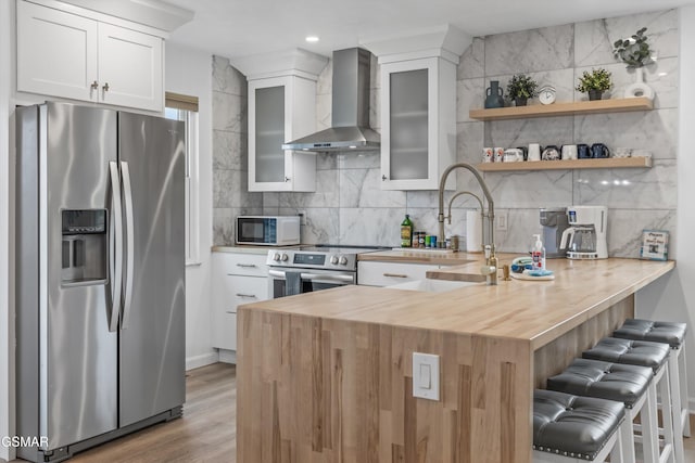 kitchen with white cabinets, wall chimney exhaust hood, backsplash, a breakfast bar, and appliances with stainless steel finishes