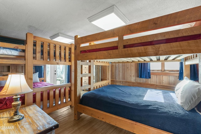 bedroom with a textured ceiling, wooden walls, and wood finished floors