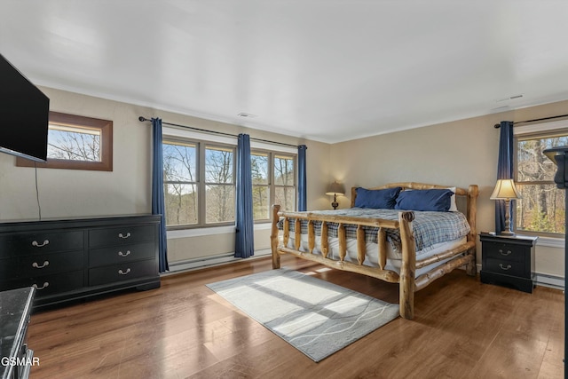 bedroom with visible vents, baseboard heating, and wood finished floors