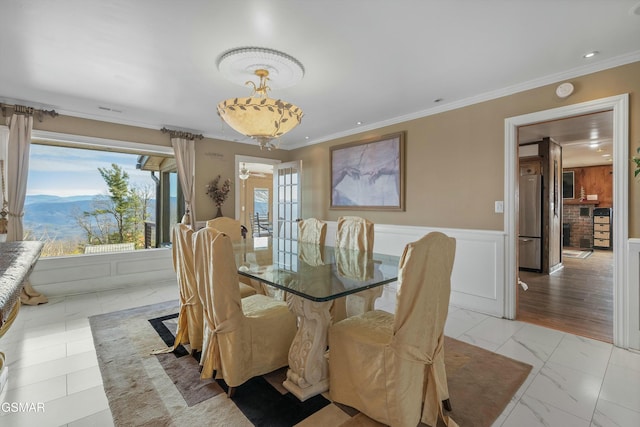 dining room featuring ornamental molding, marble finish floor, wainscoting, and a mountain view